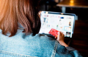 Mulher segurando cartão de crédito e navegando em site de compras no laptop, pensando em como aproveitar as ofertas da Black Friday. Representação de decisão de compra e planejamento para aproveitar promoções de Black Friday
