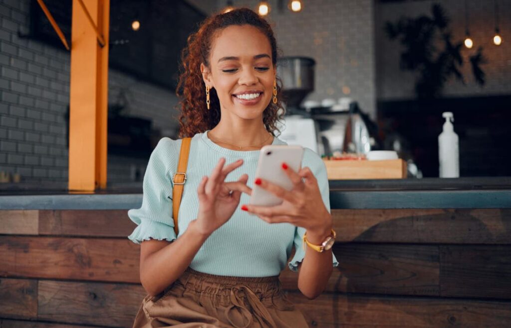 Mulher sorridente usando celular para aproveitar descontos ao pagar multas de trânsito online.