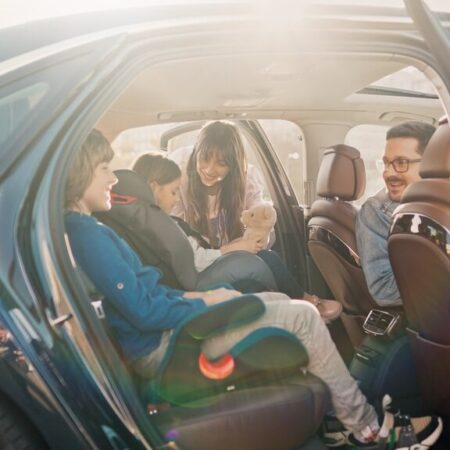 Família sorridente dentro do carro durante viagem de feriado, com crianças em cadeirinhas de segurança