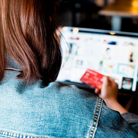 Mulher segurando cartão de crédito e navegando em site de compras no laptop, pensando em como aproveitar as ofertas da Black Friday. Representação de decisão de compra e planejamento para aproveitar promoções de Black Friday