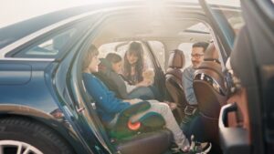 Família sorridente dentro do carro durante viagem de feriado, com crianças em cadeirinhas de segurança
