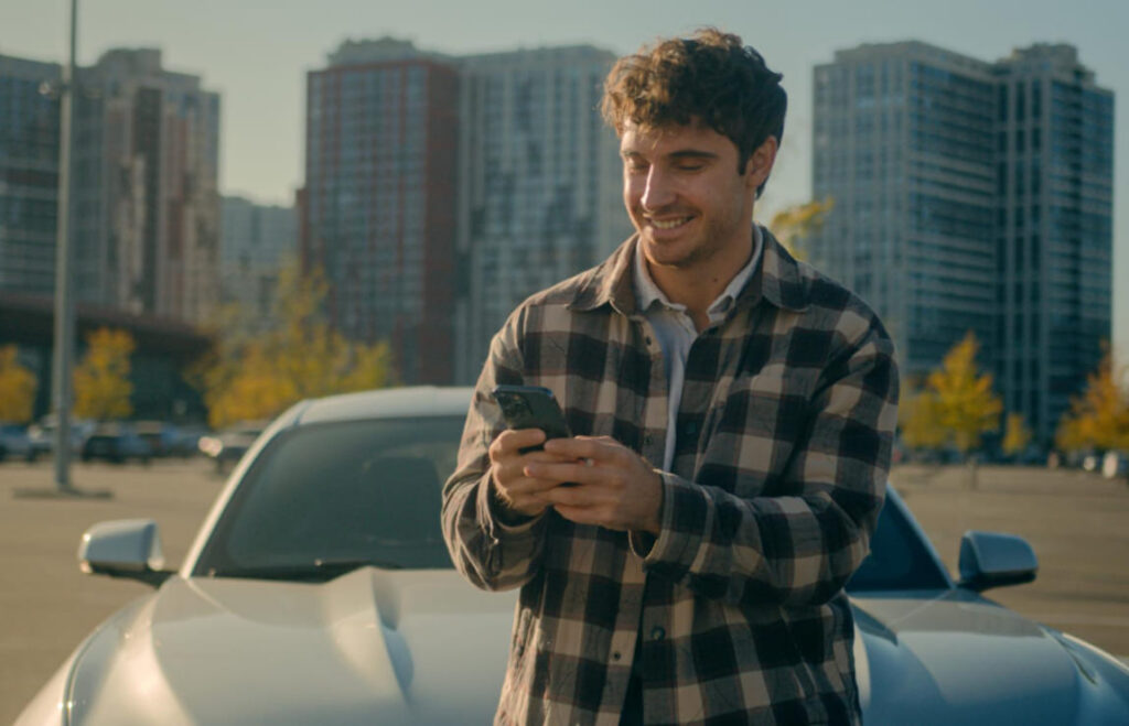 Homem motorista segurando celular e documento para realizar a IPVA 2026 consulta