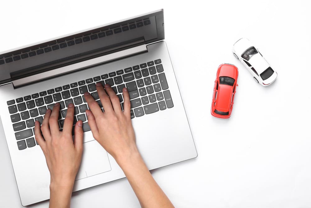 Pessoa realizando consulta sefaz ipva no notebook com documento do carro ao lado.